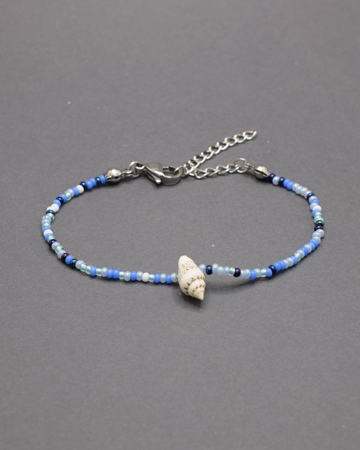 Pulseira com búzio natural e missangas de vidro em azul profundo, moderna e marcante, perfeita para um estilo autêntico com destaque subtil.