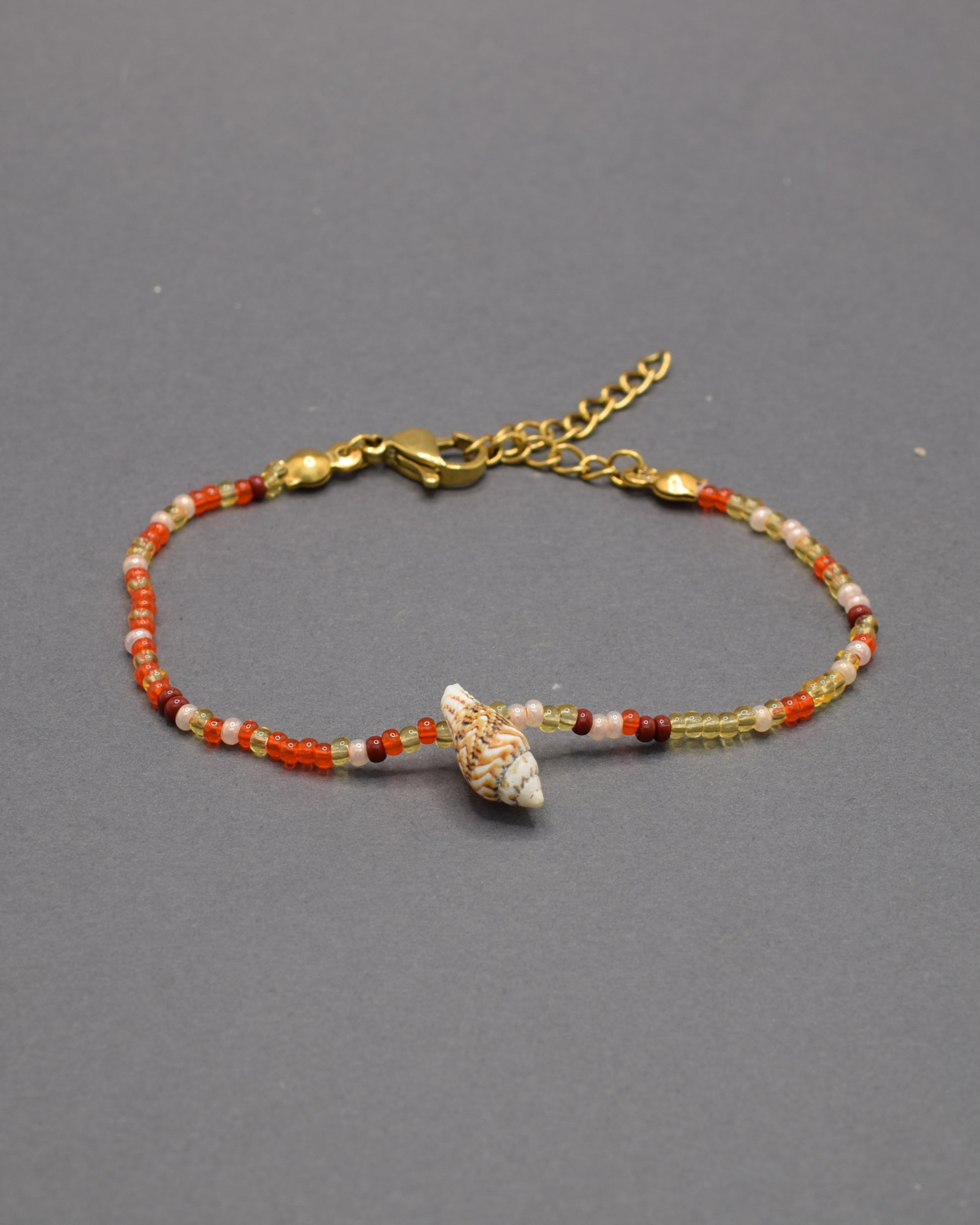 Pulseira com búzio natural e missangas de vidro em tons vermelho-alaranjado, vibrante e única, trazendo cor e personalidade ao visual.