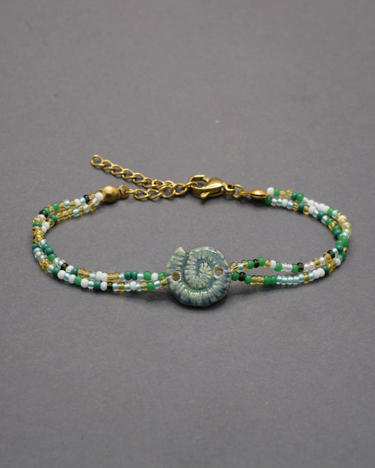 Pulseira com pendente de cerâmica caracol verde musgo, delicada e natural, perfeita para um toque original e elegante no teu look diário.