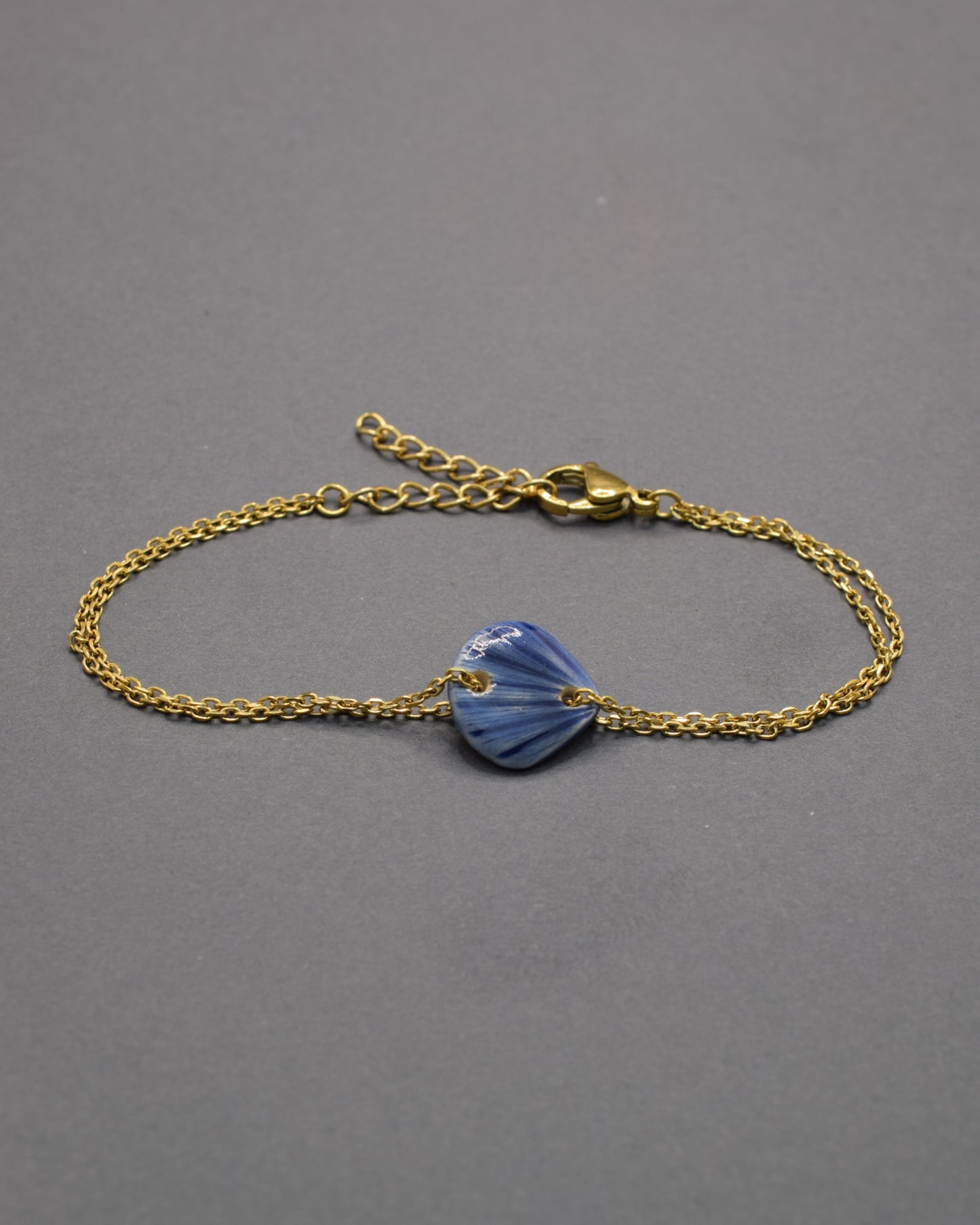 Pulseira com pendente de cerâmica em forma de concha azul escuro, elegante e sofisticada, ideal para um toque marítimo e refinado no seu look.