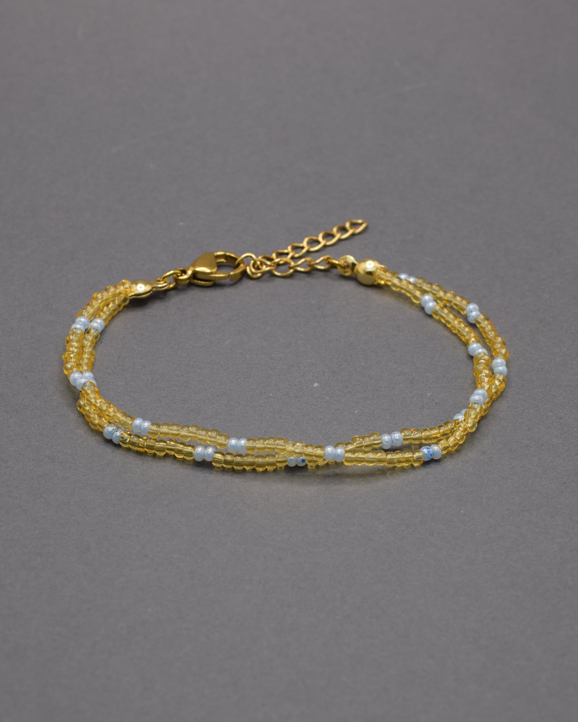 Pulseira dupla de missangas semitransparentes douradas, padrão azul claro. Irradia luz, serenidade e sofisticação com delicadeza subtil.