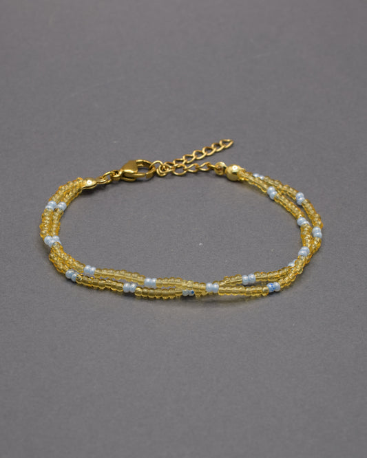 Pulseira dupla de missangas semitransparentes douradas, padrão azul claro. Irradia luz, serenidade e sofisticação com delicadeza subtil.