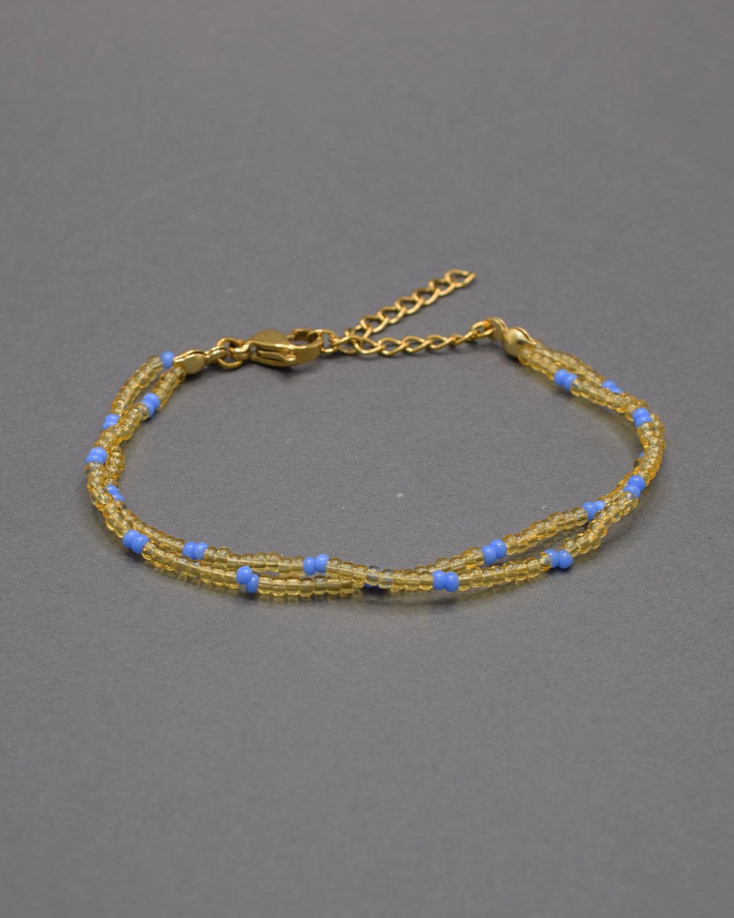 Pulseira dupla com missangas douradas semitransparentes e padrão azul neon. Design moderno e elegante para um look vibrante.