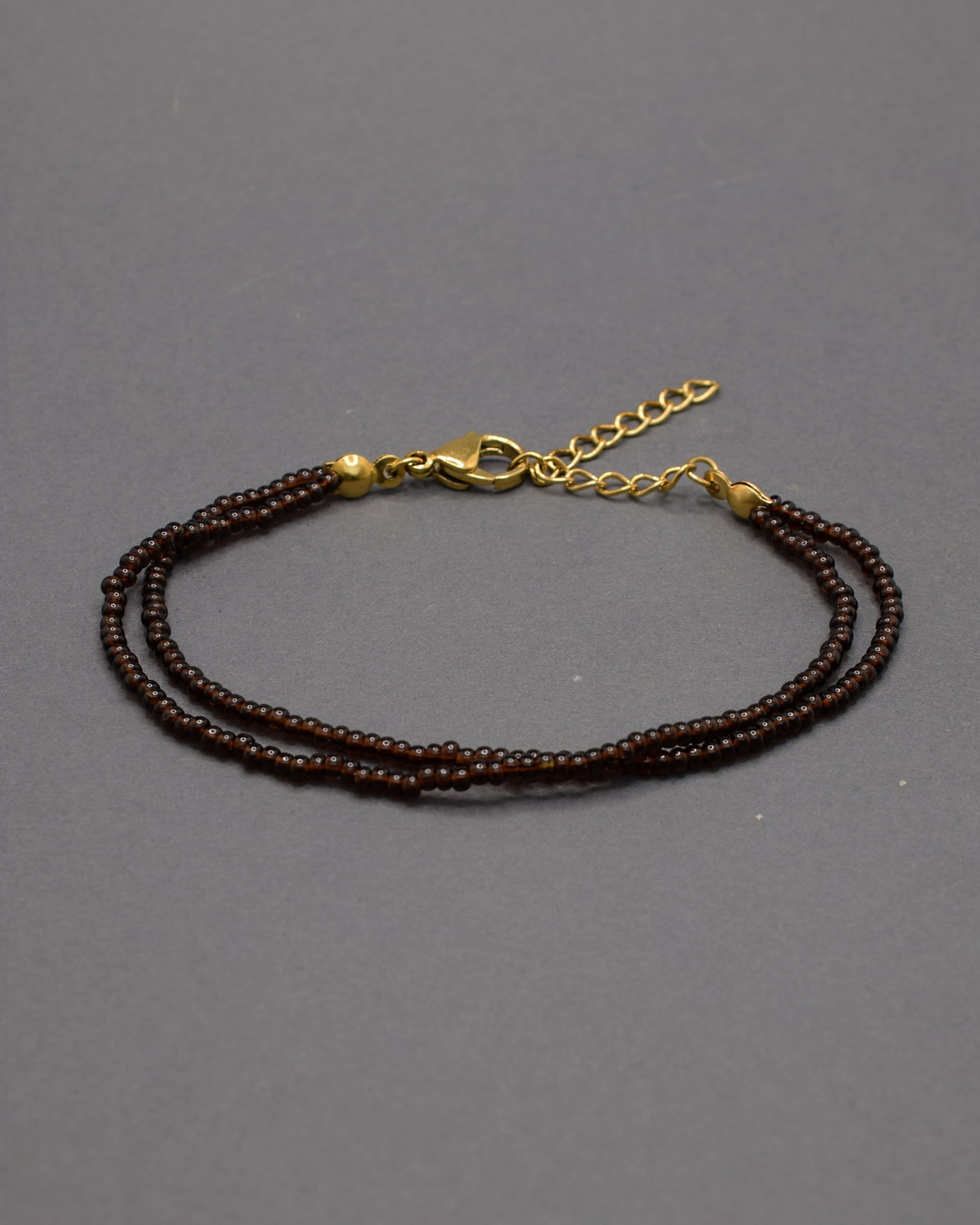 Pulseira dupla com missangas castanhas semitransparentes. Design artesanal e elegante para um toque sofisticado no seu look.