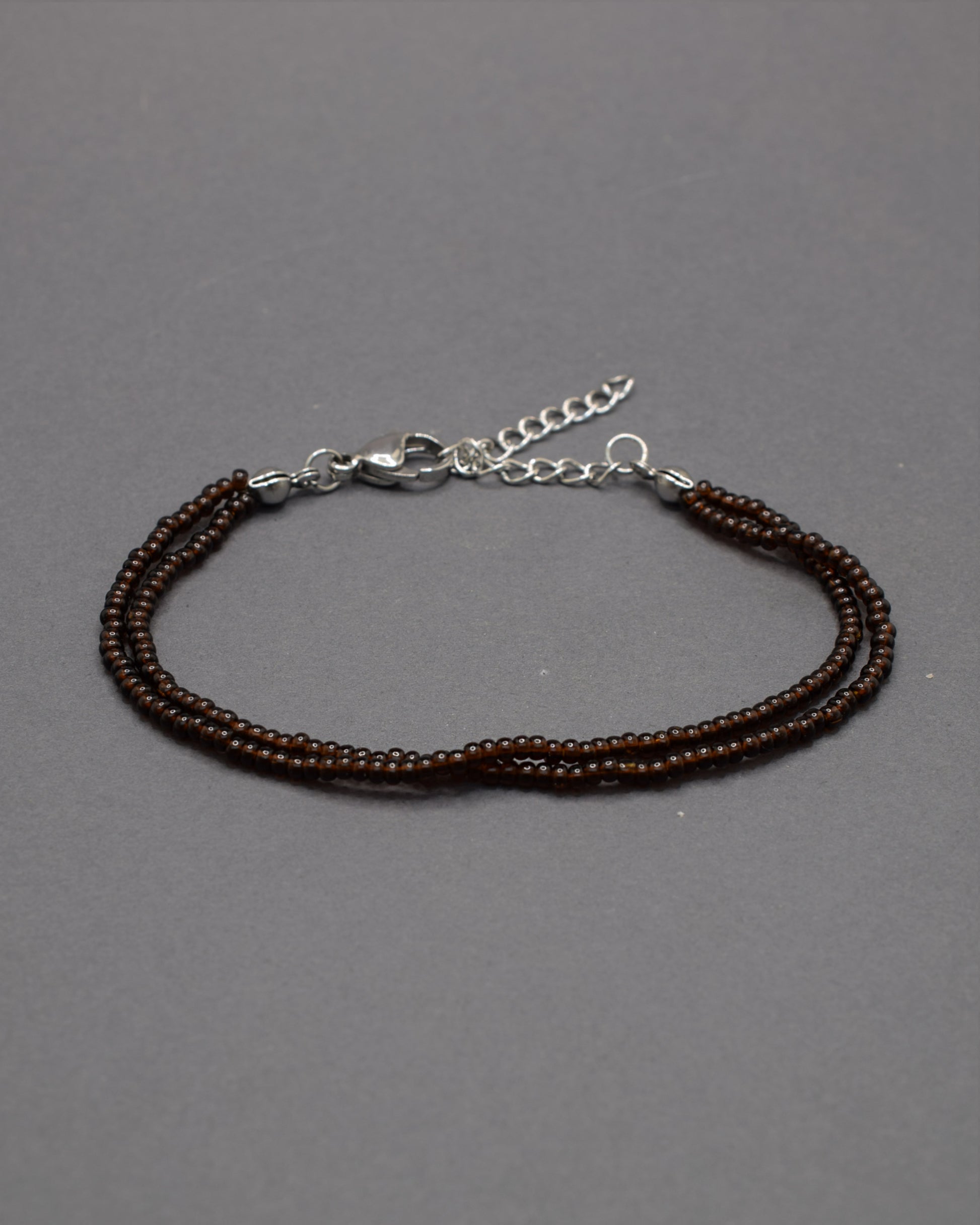 Pulseira dupla com missangas castanhas semitransparentes. Design artesanal e elegante para um toque sofisticado no seu look.