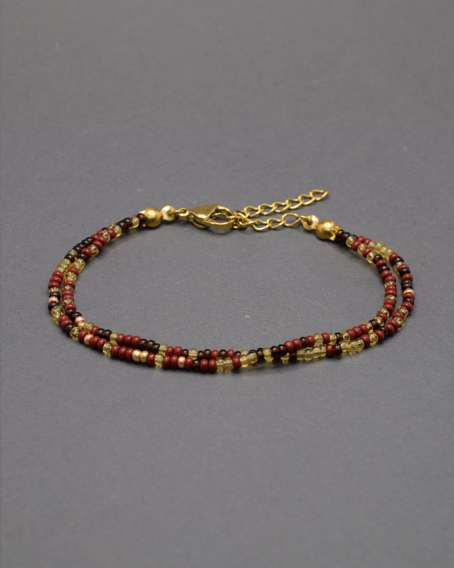 Pulseira dupla de missangas em mix bordô. Design artesanal sofisticado, ideal para um toque de cor elegante e versátil no teu look.