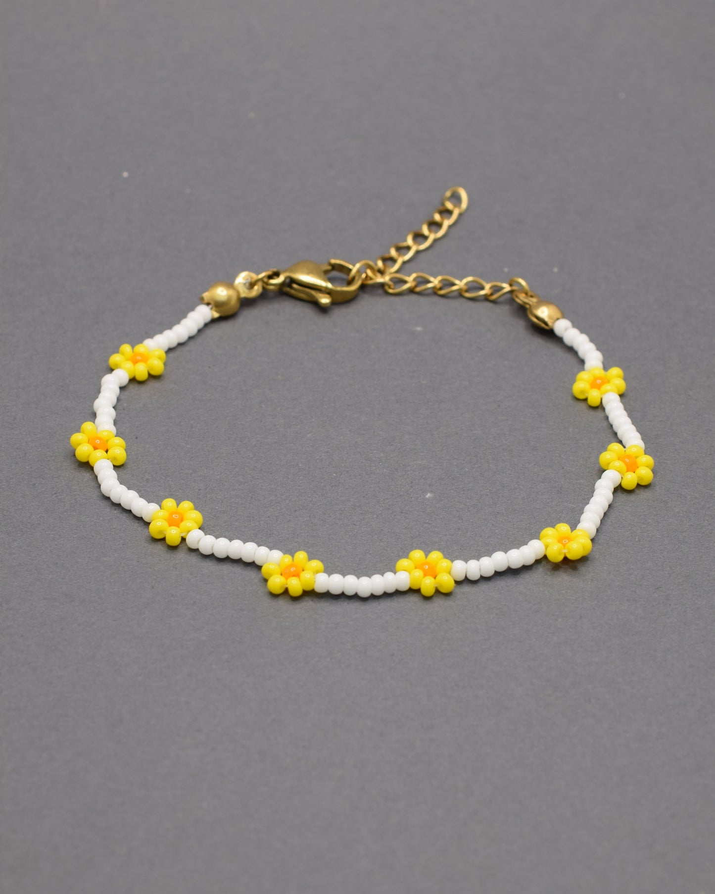 Pulseira delicada com flores amarelas feitas de missangas, sobre base de missangas brancas, perfeita para um toque alegre e artesanal ao visual.