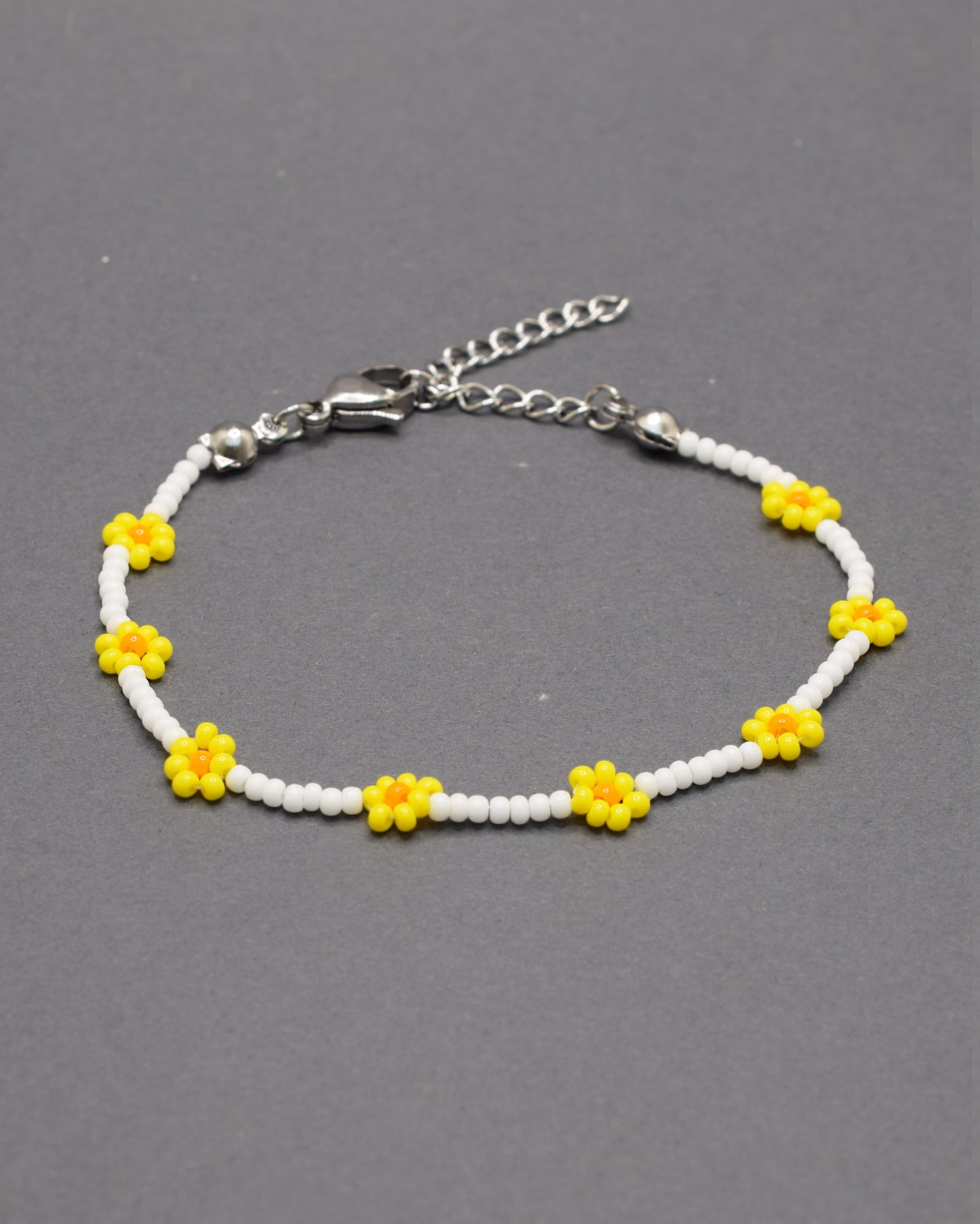 Pulseira delicada com flores amarelas feitas de missangas, sobre base de missangas brancas, perfeita para um toque alegre e artesanal ao visual.