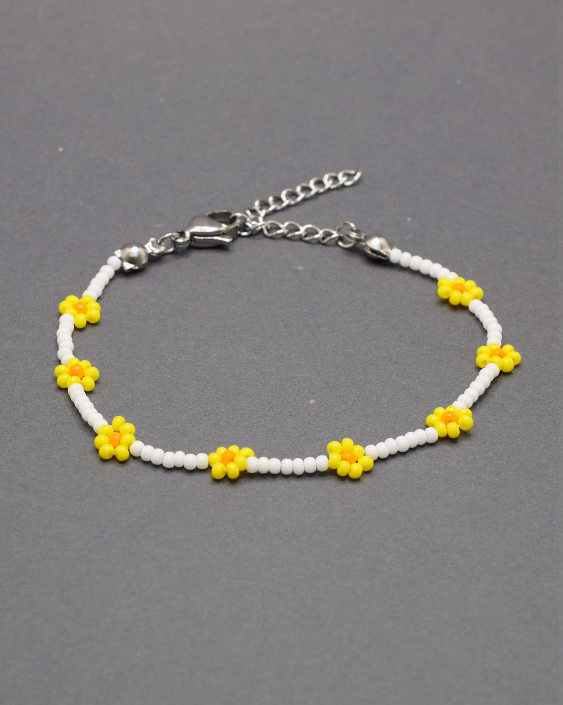 Pulseira delicada com flores amarelas feitas de missangas, sobre base de missangas brancas, perfeita para um toque alegre e artesanal ao visual.