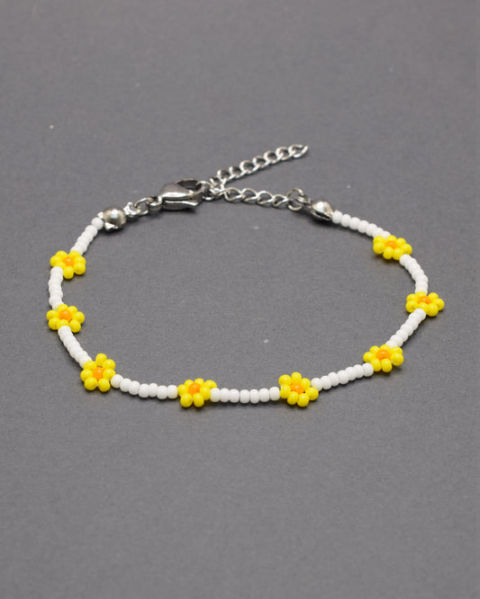 Pulseira delicada com flores amarelas feitas de missangas, sobre base de missangas brancas, perfeita para um toque alegre e artesanal ao visual.