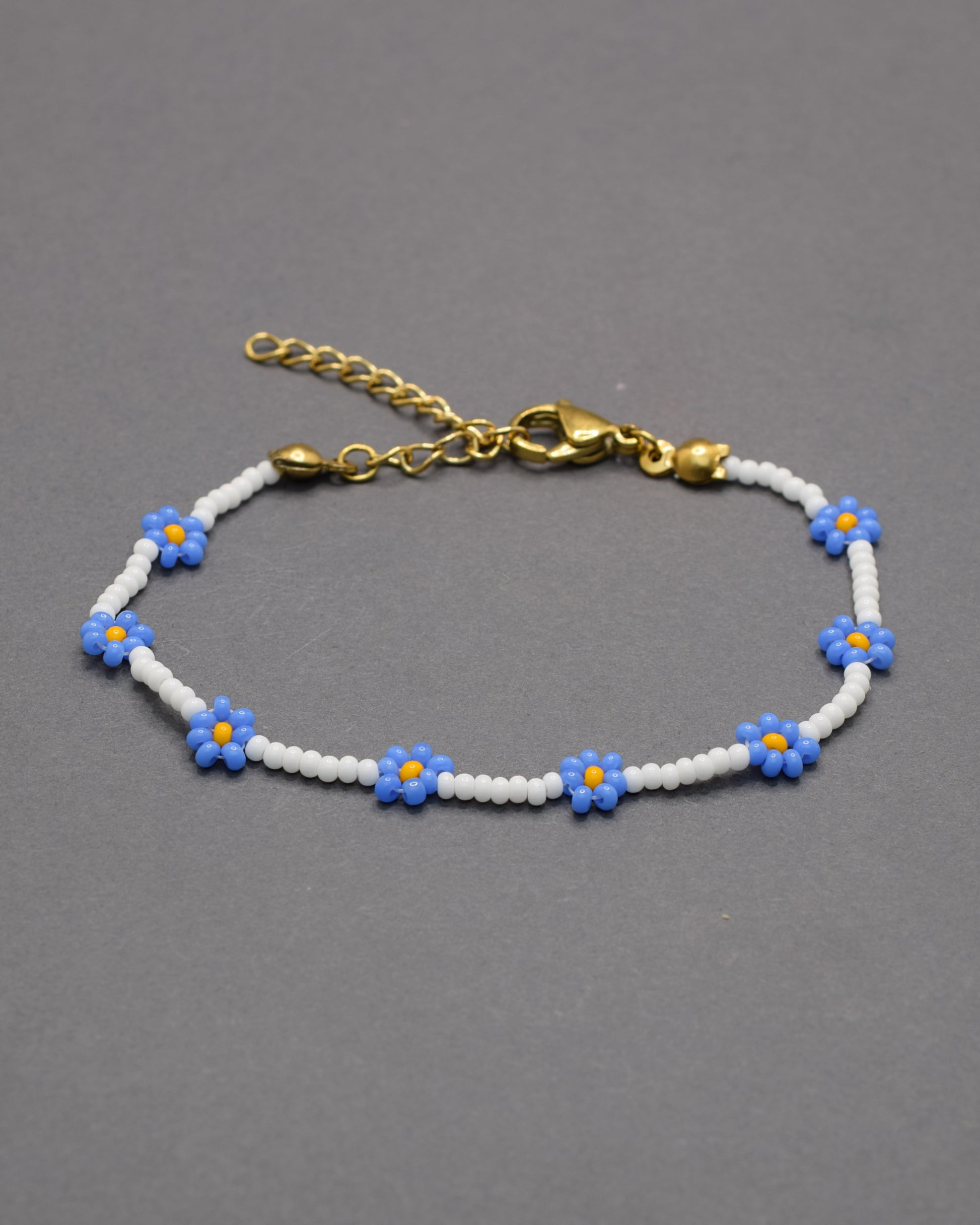 Delicada pulseira de flores azuis e missangas brancas, perfeita para dar um toque leve, elegante e fresco ao teu estilo diário.