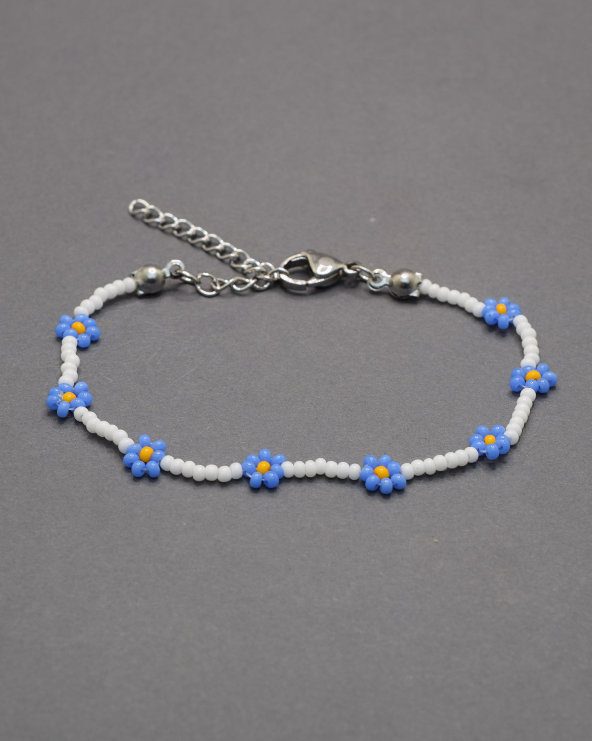 Delicada pulseira de flores azuis e missangas brancas, perfeita para dar um toque leve, elegante e fresco ao teu estilo diário.