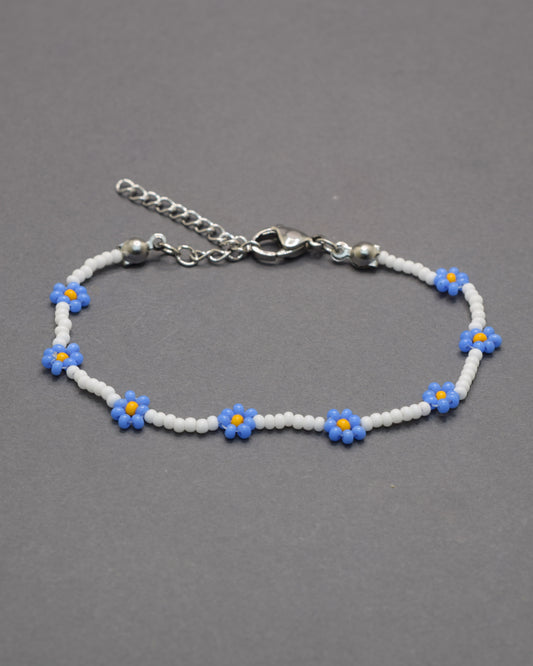Delicada pulseira de flores azuis e missangas brancas, perfeita para dar um toque leve, elegante e fresco ao teu estilo diário.