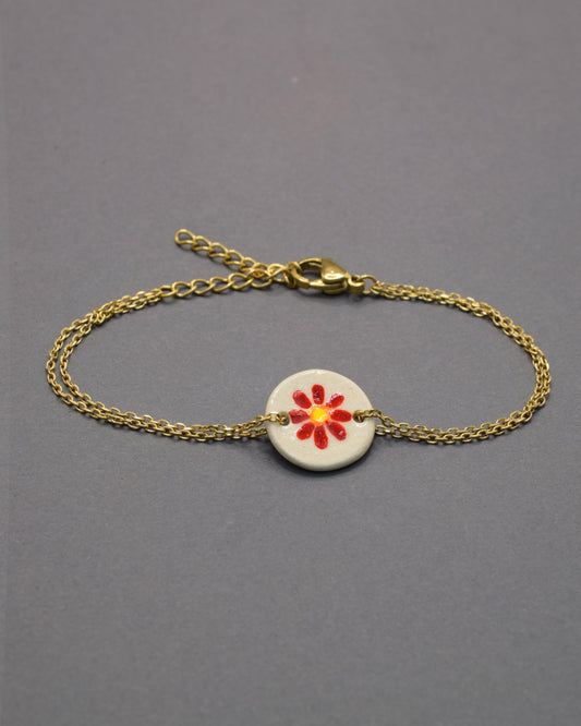 Pulseira delicada com pendente em cerâmica de margarida vermelha, vibrante e elegante, perfeita para dar um toque de cor e personalidade ao seu visual.