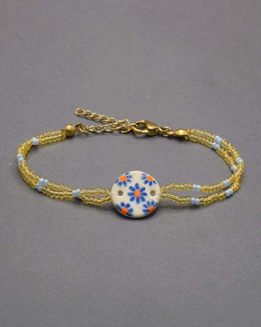 Pulseira delicada com pendente em cerâmica de margaridas azuis, leve e romântica, perfeita para dar um toque floral e encantador ao seu visual.