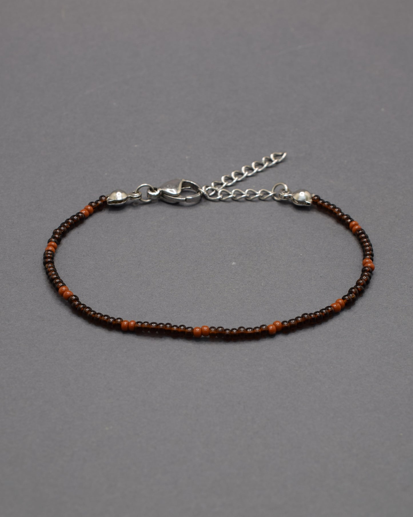 Pulseira de missangas castanhas semitransparentes com padrão castanho opaco. Elegante e versátil, ideal para um look natural e sofisticado.