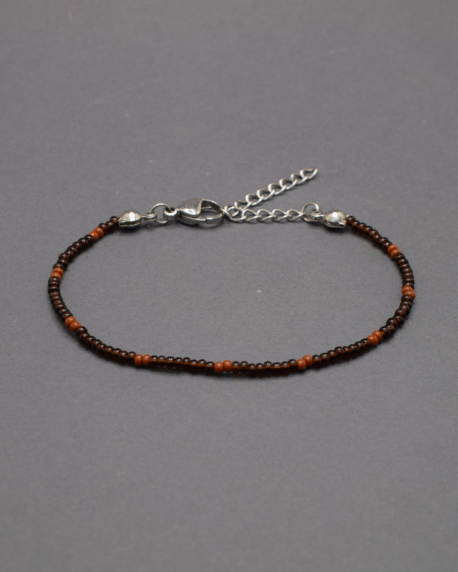 Pulseira de missangas castanhas semitransparentes com padrão castanho opaco. Elegante e versátil, ideal para um look natural e sofisticado.