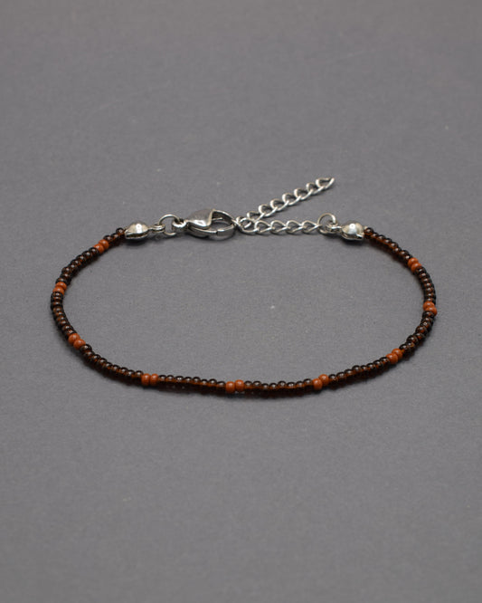 Pulseira de missangas castanhas semitransparentes com padrão castanho opaco. Elegante e versátil, ideal para um look natural e sofisticado.