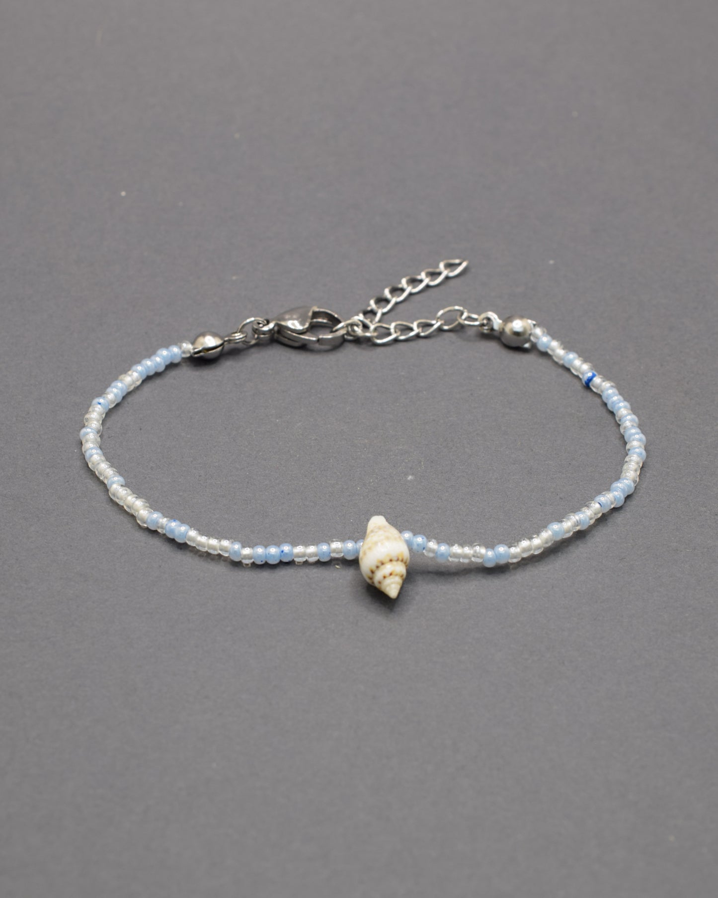 Pulseira com búzio natural e missangas de vidro em tons de azul claro, delicada e luminosa, trazendo um toque fresco e autêntico ao teu estilo.
