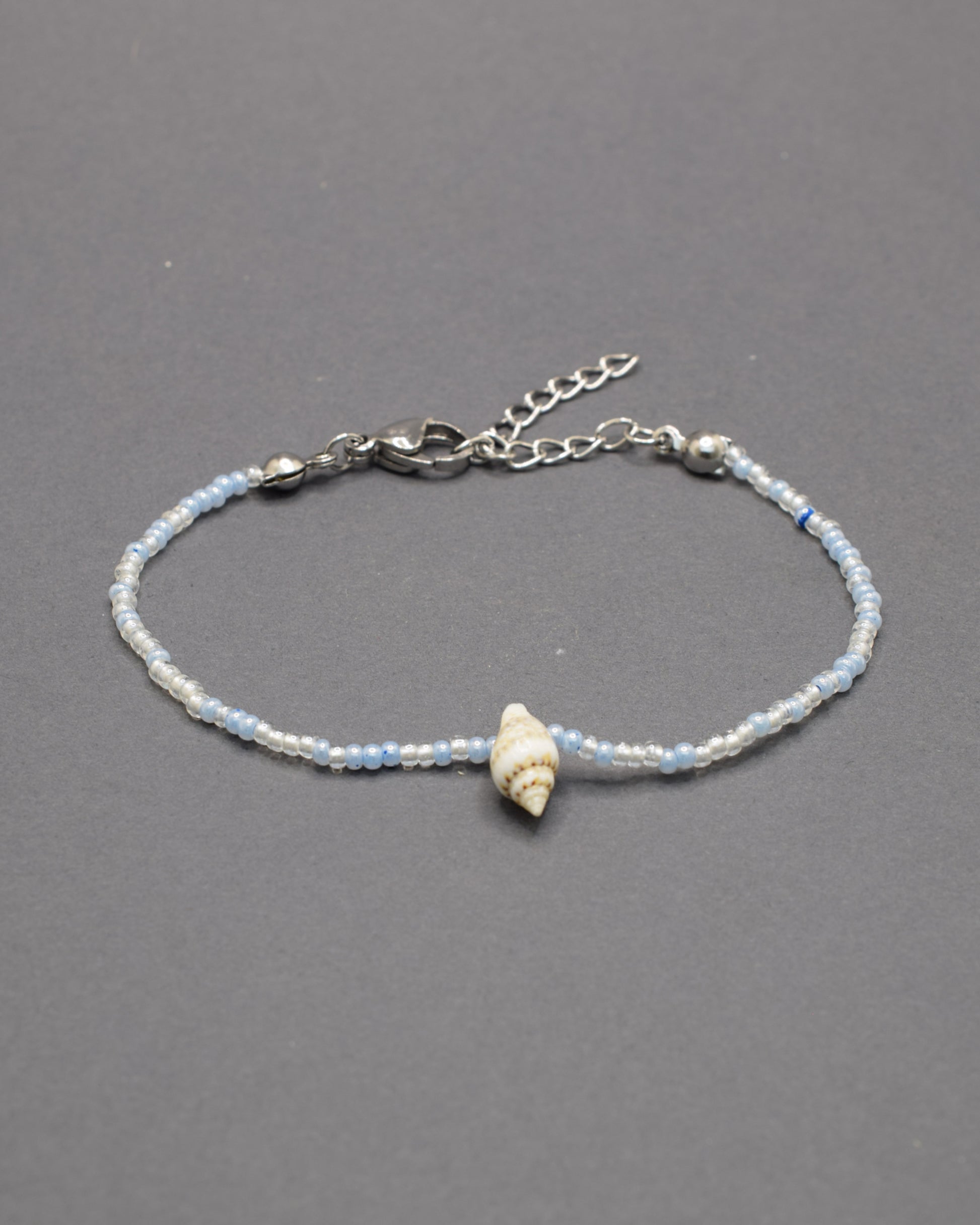 Pulseira com búzio natural e missangas de vidro em tons de azul claro, delicada e luminosa, trazendo um toque fresco e autêntico ao teu estilo.