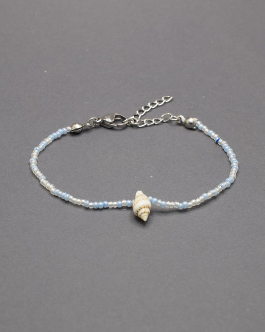 Pulseira com búzio natural e missangas de vidro em tons de azul claro, delicada e luminosa, trazendo um toque fresco e autêntico ao teu estilo.